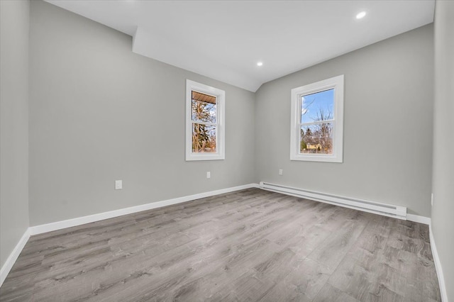 unfurnished room featuring baseboard heating, wood finished floors, baseboards, and a wealth of natural light