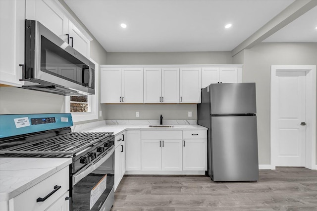 kitchen with light stone counters, white cabinetry, stainless steel appliances, light wood finished floors, and a sink