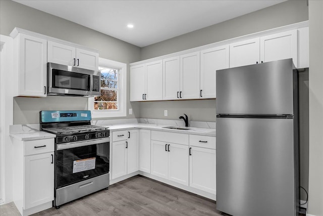 kitchen featuring white cabinets, a sink, stainless steel appliances, light wood-style flooring, and light stone counters