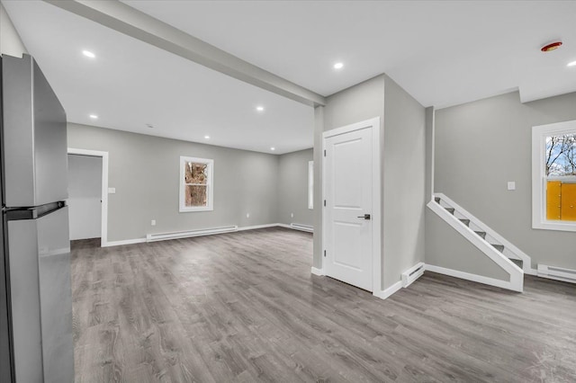 basement with a baseboard radiator, freestanding refrigerator, wood finished floors, and baseboards
