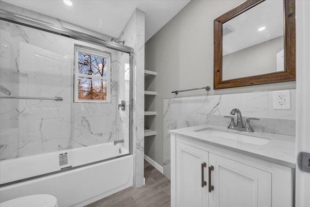 bathroom with vanity, toilet, wood finished floors, combined bath / shower with glass door, and tile walls