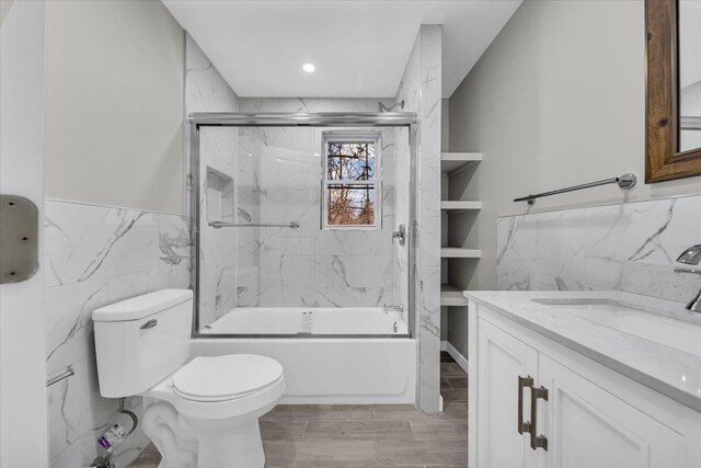 bathroom featuring shower / bath combination with glass door, vanity, a wainscoted wall, toilet, and tile walls