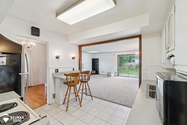 514 Chalmers St, Flint, MI 48503 - kitchen with black microwave, a chandelier, white cabinetry, light carpet, and light tile patterned floors
