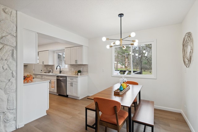 323 13th St, Plainwell, MI 49080 - kitchen featuring an inviting chandelier, dishwasher, light countertops, light wood-type flooring, and backsplash