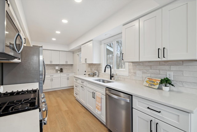 323 13th St, Plainwell, MI 49080 - kitchen with light wood-style floors, white cabinetry, light countertops, a sink, and stainless steel appliances