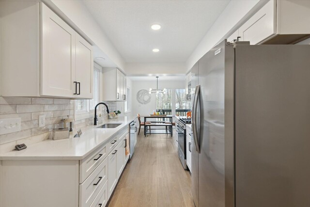 323 13th St, Plainwell, MI 49080 - kitchen featuring backsplash, white cabinets, appliances with stainless steel finishes, light wood finished floors, and a sink