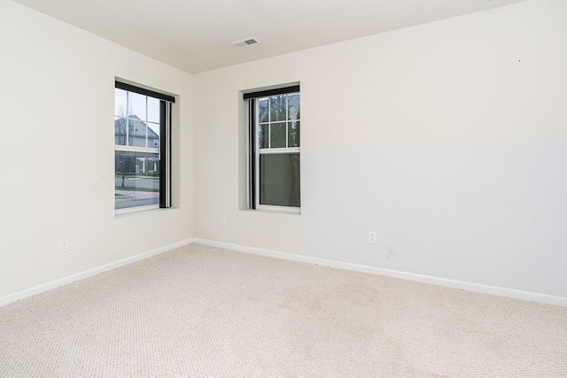 empty room with visible vents, baseboards, and light colored carpet