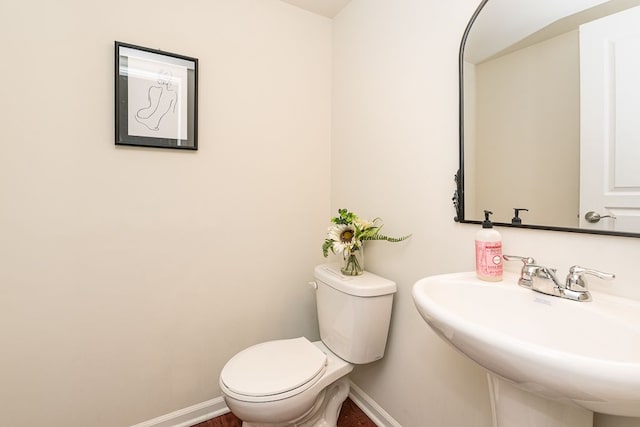 half bathroom with baseboards, a sink, and toilet