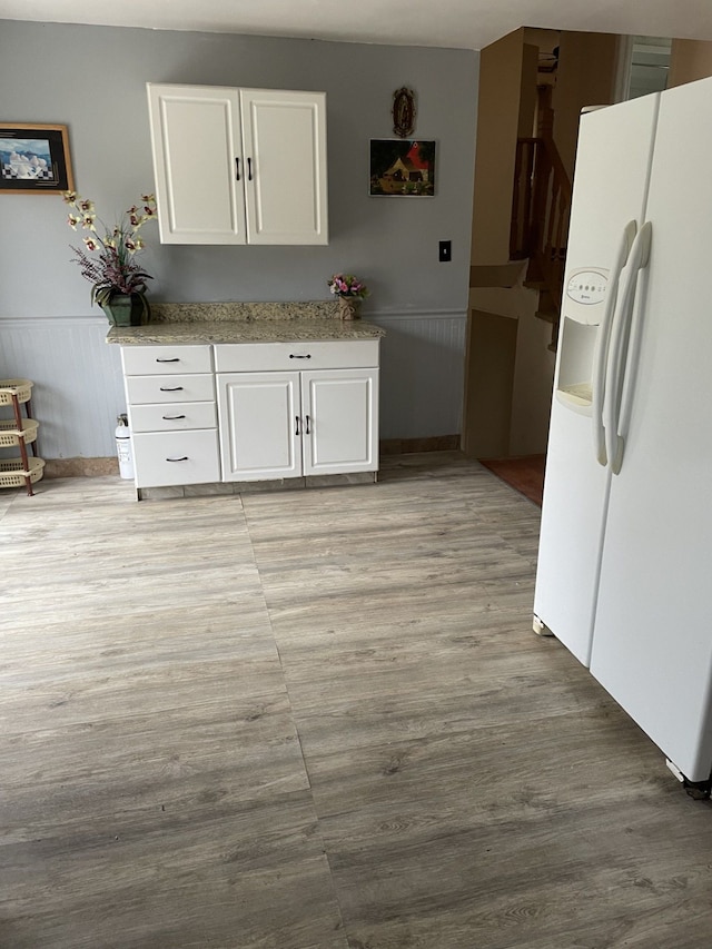 interior space with light wood-type flooring, white fridge with ice dispenser, white cabinets, and a wainscoted wall