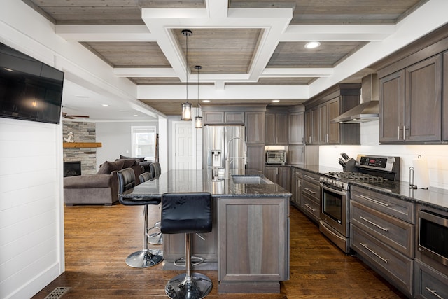 kitchen with wall chimney exhaust hood, dark wood-type flooring, dark stone countertops, a sink, and stainless steel appliances