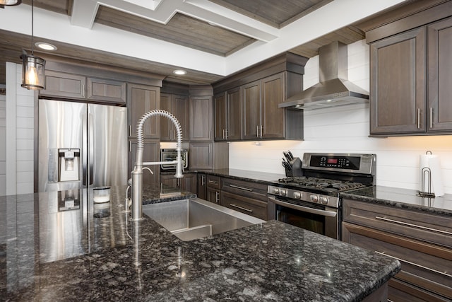 kitchen with wall chimney range hood, decorative light fixtures, beam ceiling, stainless steel appliances, and a sink