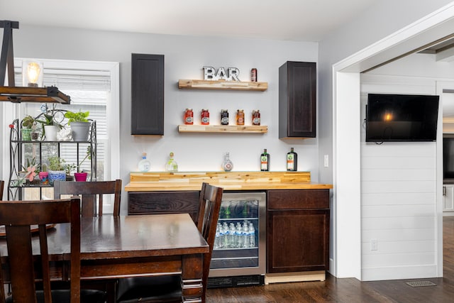 bar featuring a bar, wine cooler, and dark wood-type flooring