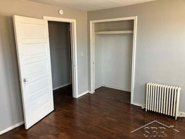 unfurnished bedroom with a closet, baseboards, radiator, and wood finished floors