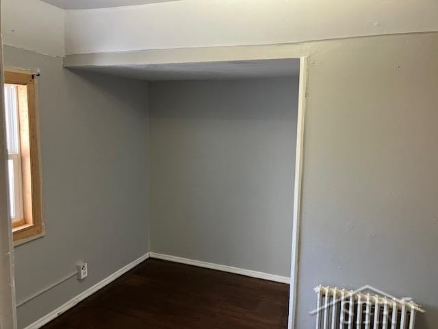 empty room featuring radiator heating unit, baseboards, and dark wood finished floors