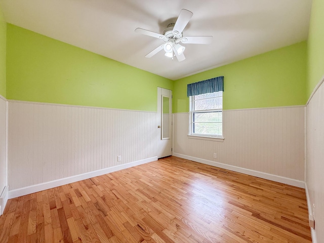 unfurnished room featuring wood finished floors, a ceiling fan, baseboards, and a wainscoted wall