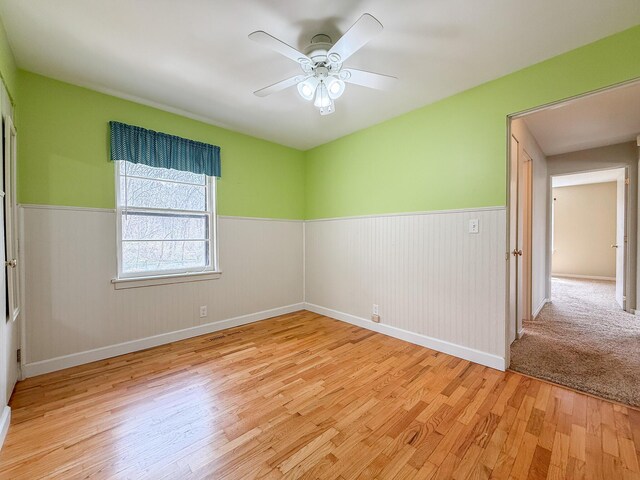 empty room featuring light wood-style floors, wainscoting, ceiling fan, and baseboards