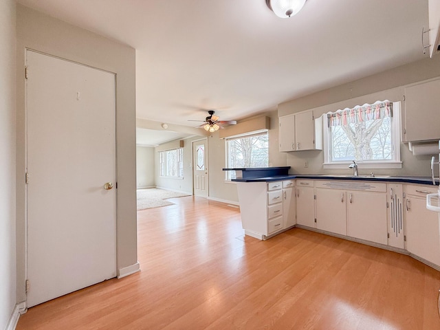 kitchen with a sink, dark countertops, ceiling fan, and light wood-style flooring