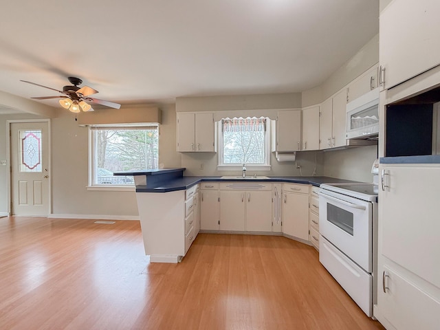 kitchen with ceiling fan, dark countertops, a sink, white appliances, and light wood-style flooring