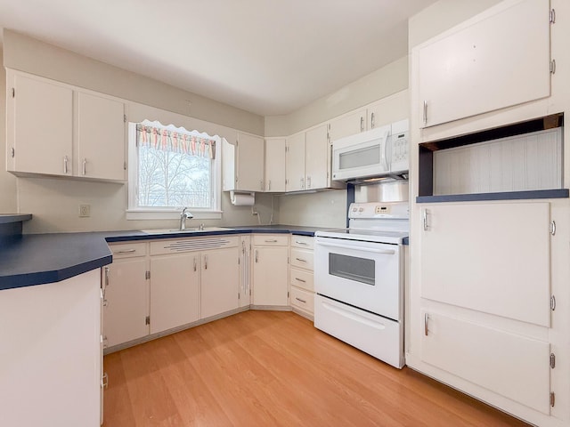 kitchen with dark countertops, a sink, light wood-style floors, white appliances, and white cabinetry