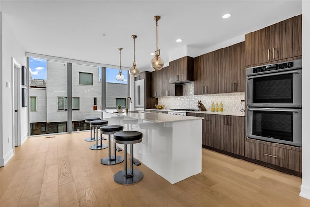 248 Alfred St, Detroit, MI 48201 - kitchen featuring decorative backsplash, stainless steel double oven, a center island with sink, light countertops, and light wood-style flooring