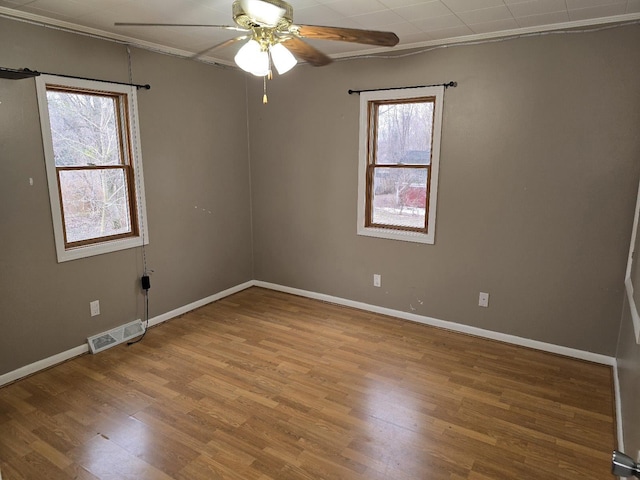 unfurnished room with a wealth of natural light, visible vents, wood finished floors, and ceiling fan
