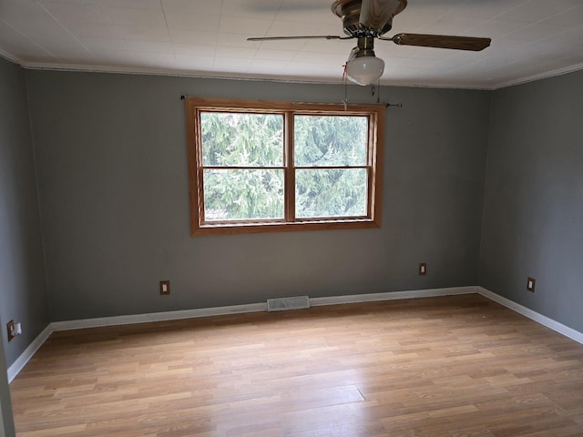 spare room featuring light wood-type flooring, visible vents, crown molding, ceiling fan, and baseboards
