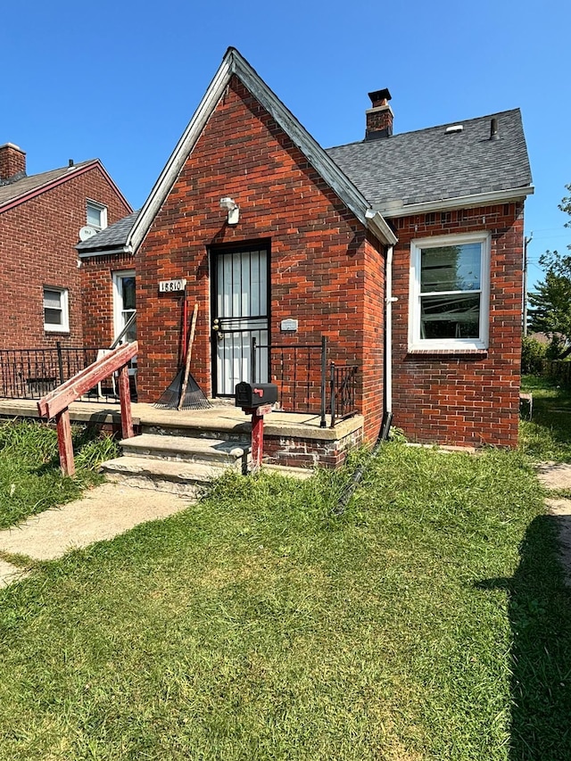 view of front of property with a chimney, a shingled roof, a front yard, and brick siding