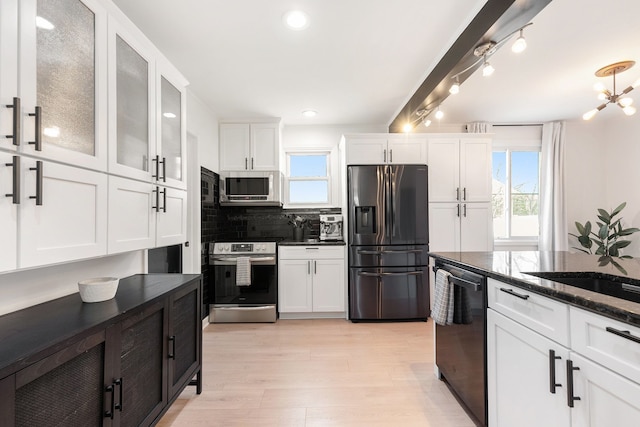 kitchen with light wood-style flooring, white cabinets, dark stone countertops, appliances with stainless steel finishes, and backsplash