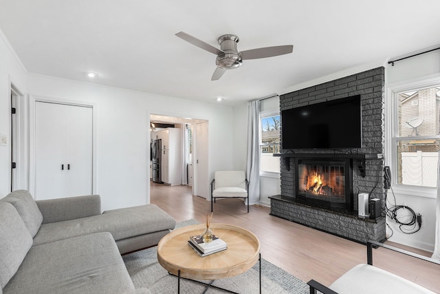 living room with a brick fireplace, ceiling fan, baseboards, and wood finished floors