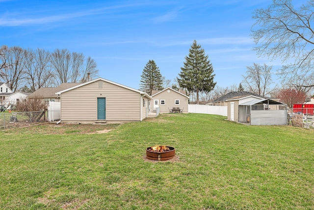 rear view of house featuring an outbuilding, a fenced backyard, a fire pit, and a lawn