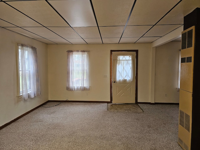 carpeted spare room with a paneled ceiling, a heating unit, and plenty of natural light