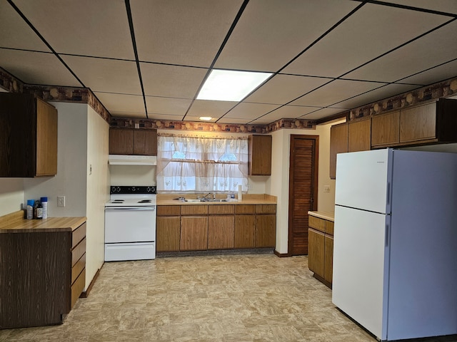 kitchen with range hood, a sink, white appliances, a drop ceiling, and light floors