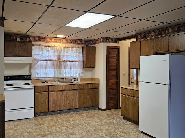 kitchen with a paneled ceiling, white appliances, under cabinet range hood, light countertops, and a sink