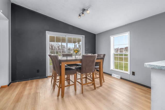 dining space featuring a textured ceiling, visible vents, lofted ceiling, light wood finished floors, and baseboards