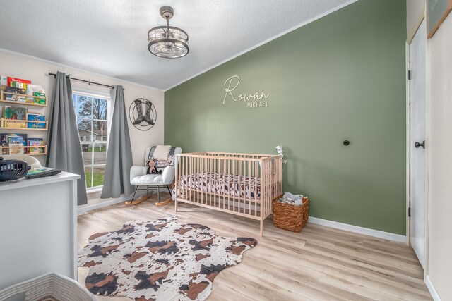 bedroom with ornamental molding, wood finished floors, lofted ceiling, a crib, and baseboards