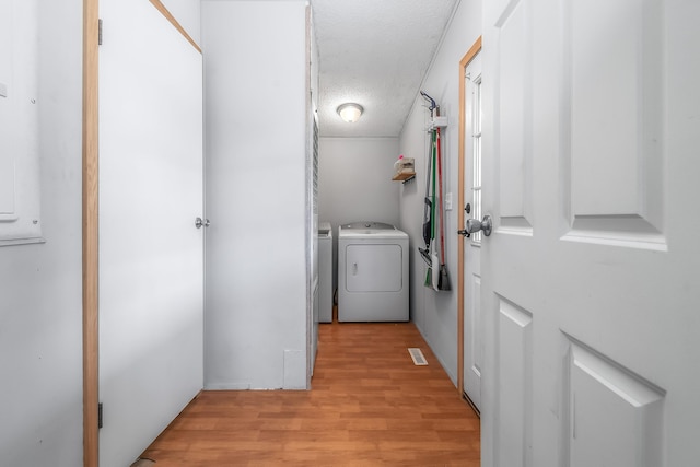 laundry room featuring a textured ceiling, visible vents, laundry area, light wood finished floors, and washing machine and clothes dryer
