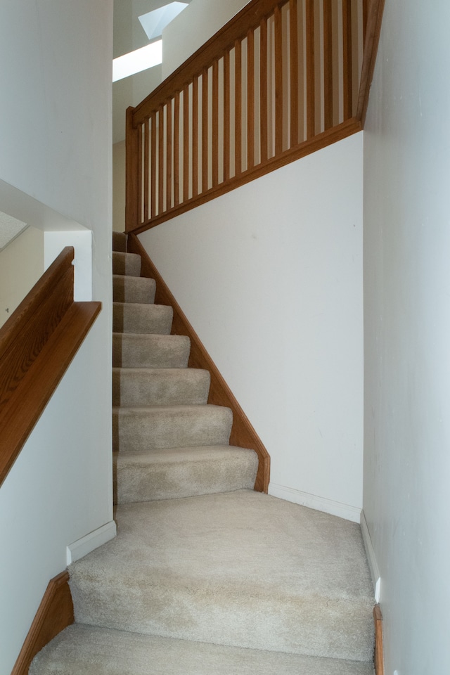 stairway featuring a skylight, carpet flooring, and baseboards