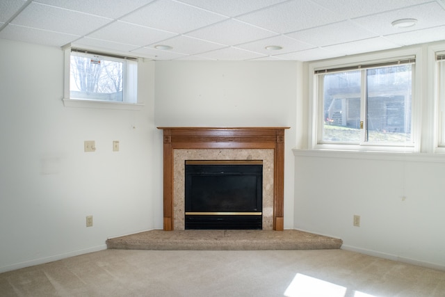 unfurnished living room with a drop ceiling, plenty of natural light, baseboards, a glass covered fireplace, and carpet floors