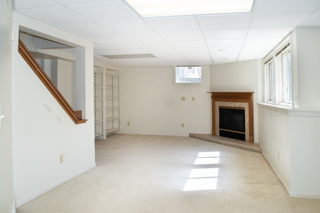 unfurnished living room with a paneled ceiling, carpet floors, stairway, baseboards, and a glass covered fireplace