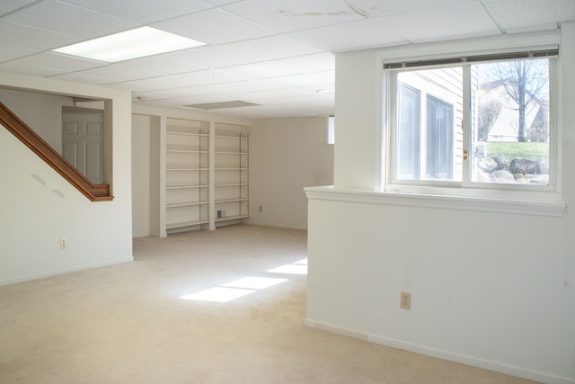 below grade area with a paneled ceiling, carpet floors, and baseboards