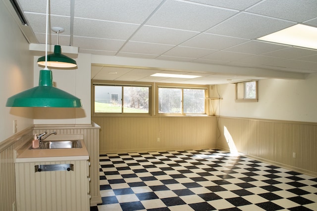 below grade area with a sink, tile patterned floors, a wainscoted wall, and a drop ceiling