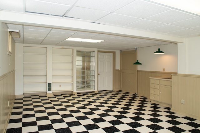 unfurnished room featuring a wainscoted wall, a drop ceiling, and tile patterned floors