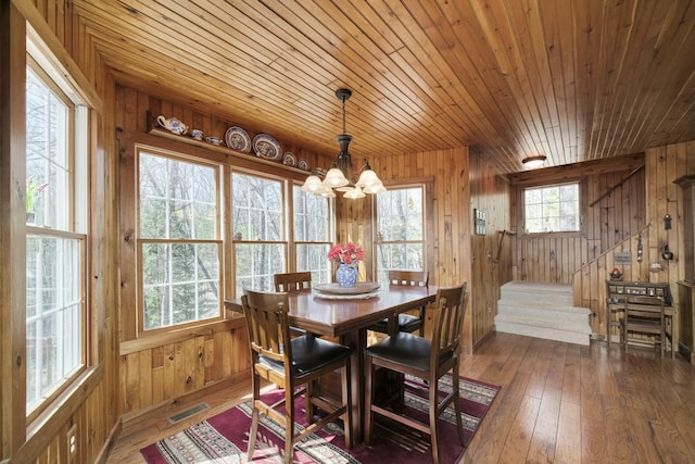 dining room with a chandelier, wooden walls, visible vents, and hardwood / wood-style floors