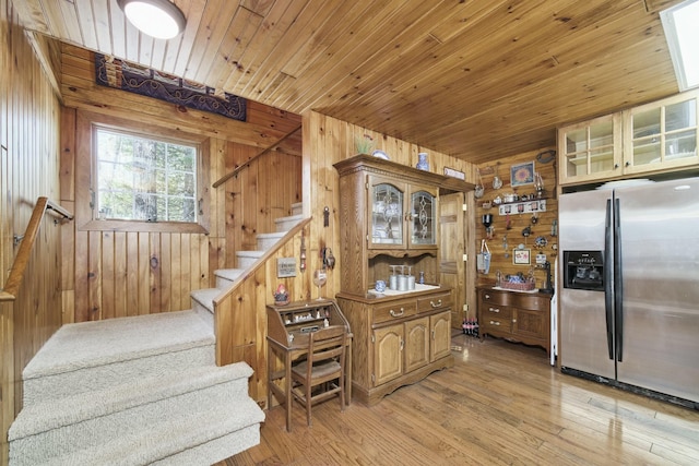 kitchen featuring stainless steel fridge with ice dispenser, glass insert cabinets, light wood-style flooring, wood walls, and wood ceiling