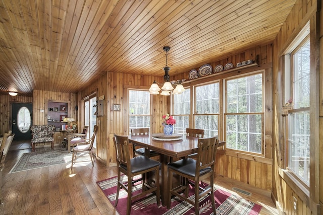 dining area with an inviting chandelier, wood walls, visible vents, hardwood / wood-style floors, and wooden ceiling
