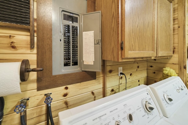clothes washing area with electric panel, wooden walls, washer and clothes dryer, and cabinet space