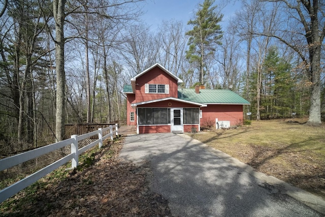 view of front of home featuring a sunroom, a chimney, aphalt driveway, and fence