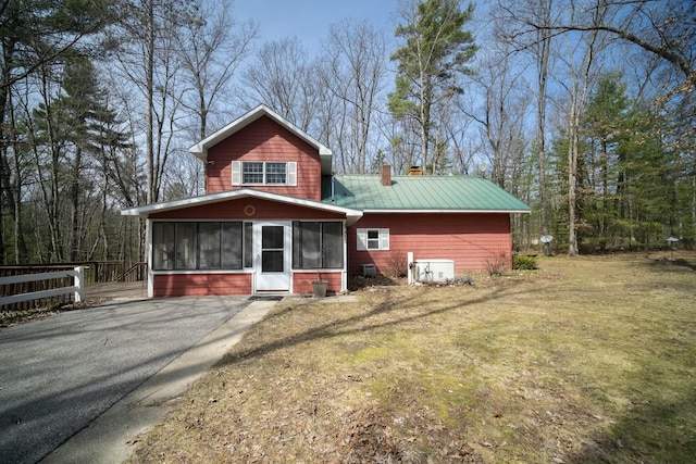 exterior space featuring metal roof, a sunroom, a lawn, and a chimney