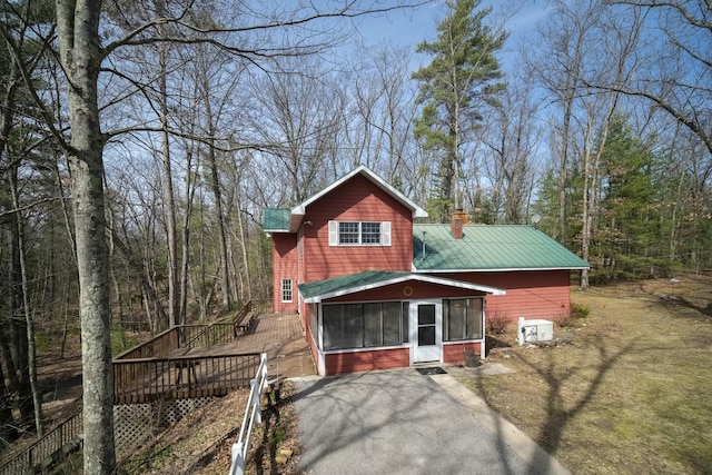 rear view of property with a sunroom, a chimney, metal roof, and a deck