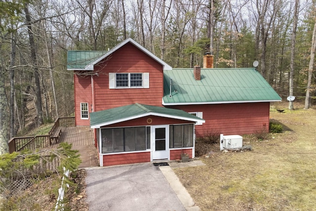 chalet / cabin featuring a forest view, metal roof, a sunroom, and a chimney